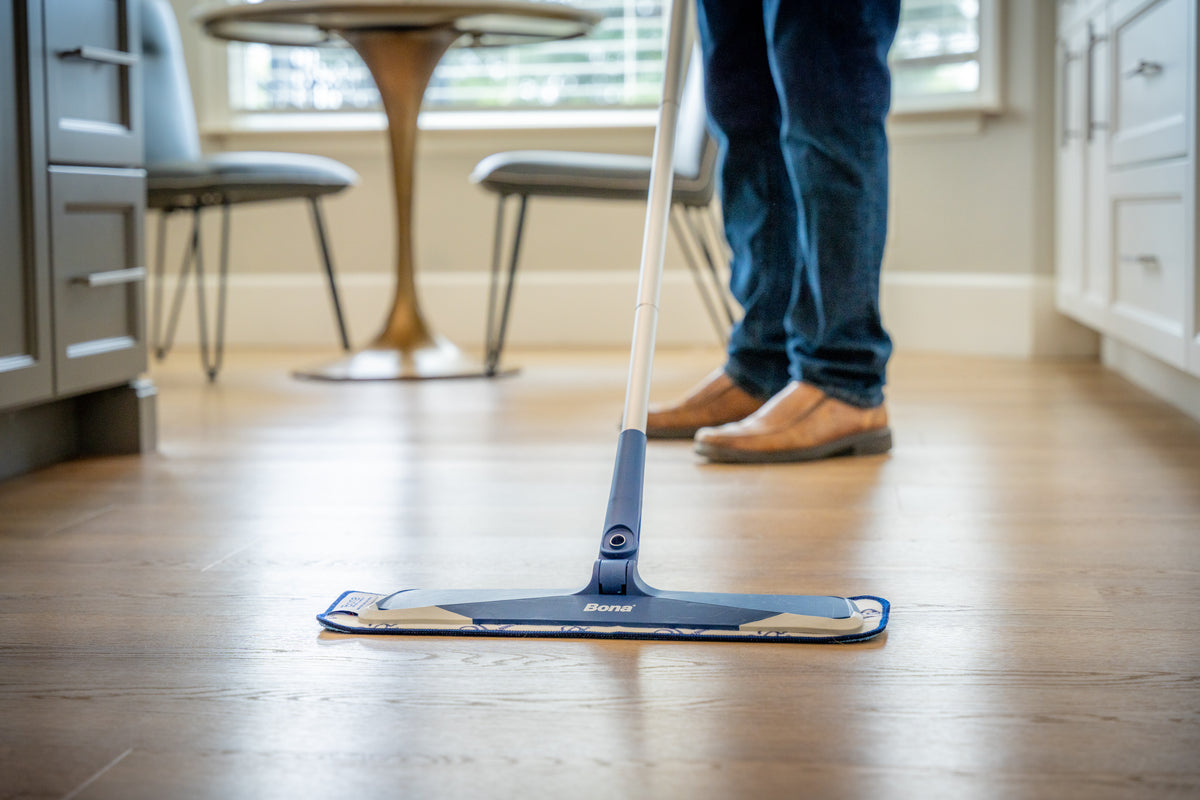 Person cleaning light oak hardwood flooring with a flat microfiber mop in a kitchen