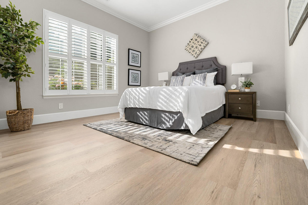Light oak wood flooring in a modern bedroom with a gray upholstered bed and patterned area rug.