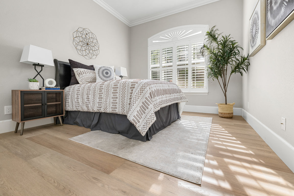 Light oak wood flooring in a styled bedroom with a light area rug and geometric patterned bedding.