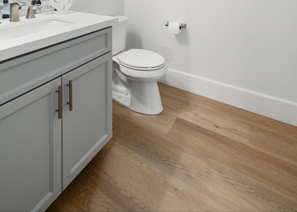 Light brown wood-look plank flooring in a modern bathroom with a light gray vanity and white toilet.