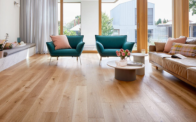 Natural hardwood flooring in a modern living room featuring two teal chairs and a beige sofa.