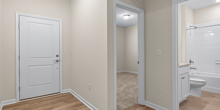 Wood-look plank flooring in a rental unit hallway leading to a carpeted bedroom and bathroom