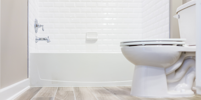 Light wood-look vinyl plank flooring in a bathroom with a white tub and subway tile surround