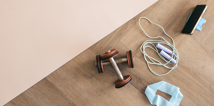 Dumbbells, jump rope, and a resistance band on wood-look plank flooring in a home gym
