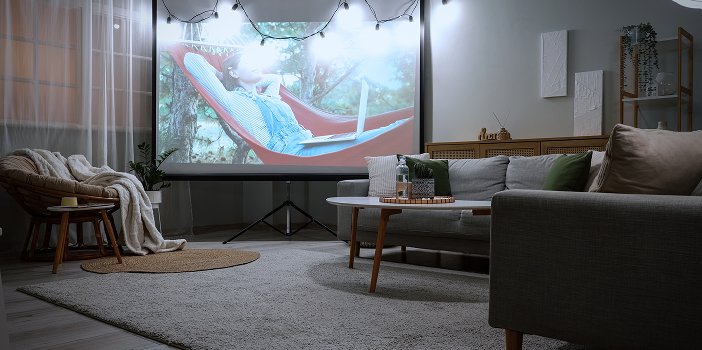 Home theater room with a projection screen, gray sectional, and plush area rug over wood flooring
