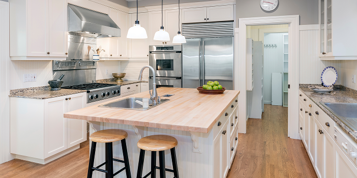 Warm oak hardwood flooring in a white kitchen with a butcher-block island and stainless appliances