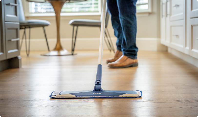 Person cleaning light oak hardwood flooring with a flat microfiber mop in a kitchen