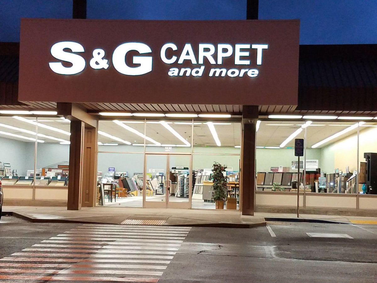 S&G Carpet and More storefront at dusk with the lit sign and flooring showroom visible through the windows