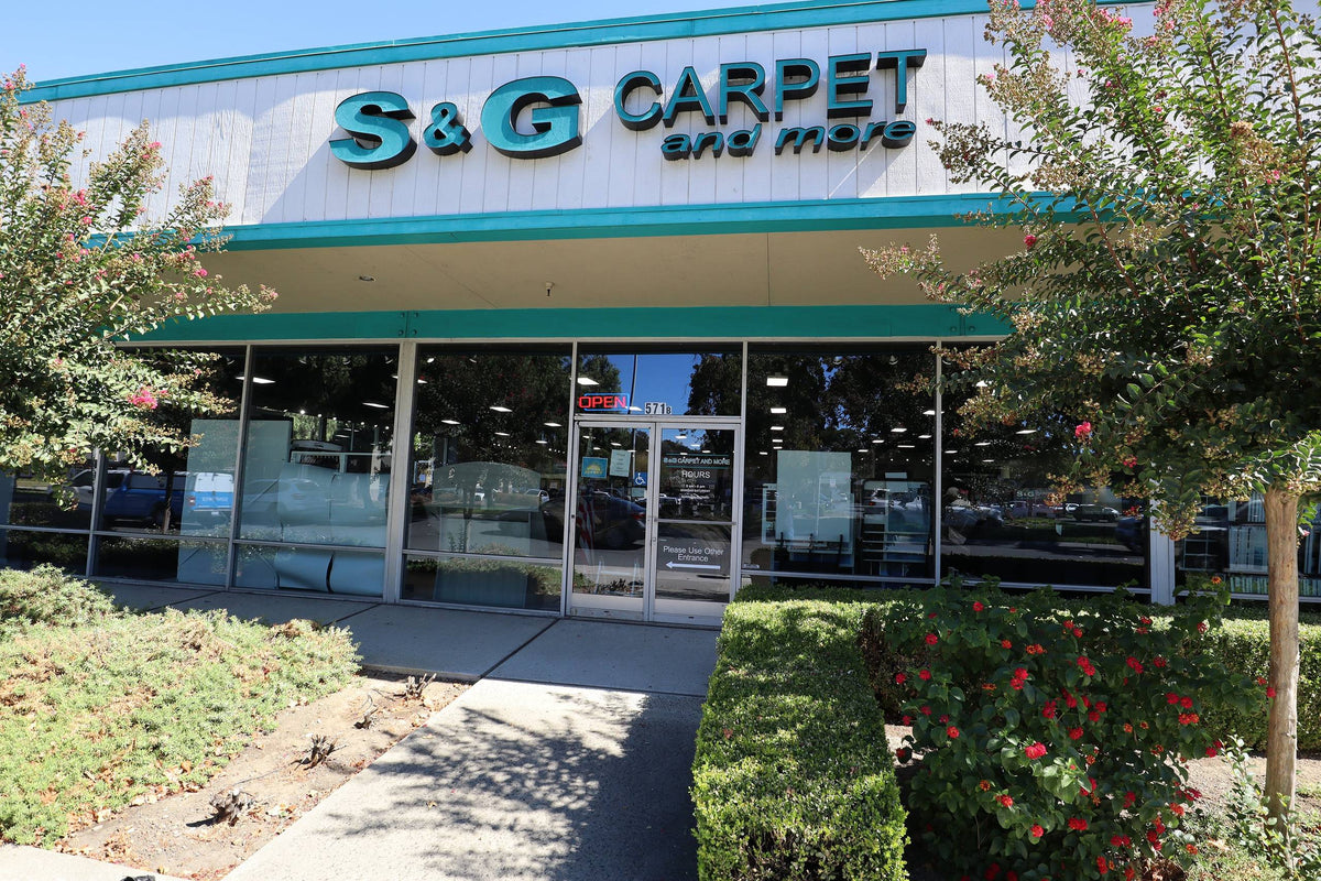 Storefront of the S&G Carpet and More showroom in Pleasant Hill with teal signage and flowering shrubs