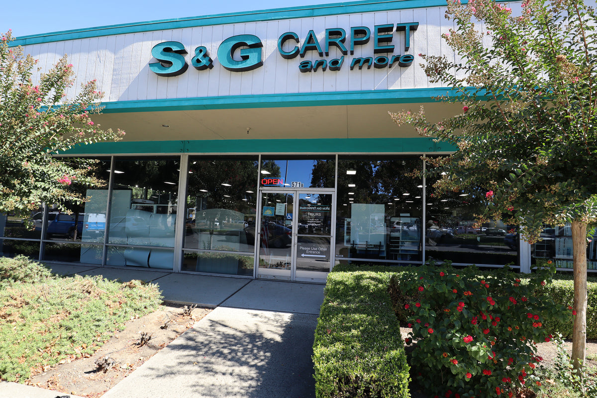 Storefront of the S&G Carpet and More showroom in Pleasant Hill with teal signage and flowering shrubs