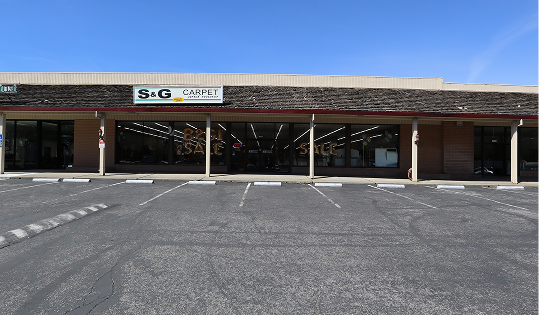 S&G Carpet storefront exterior with large glass windows and a wide paved parking lot.