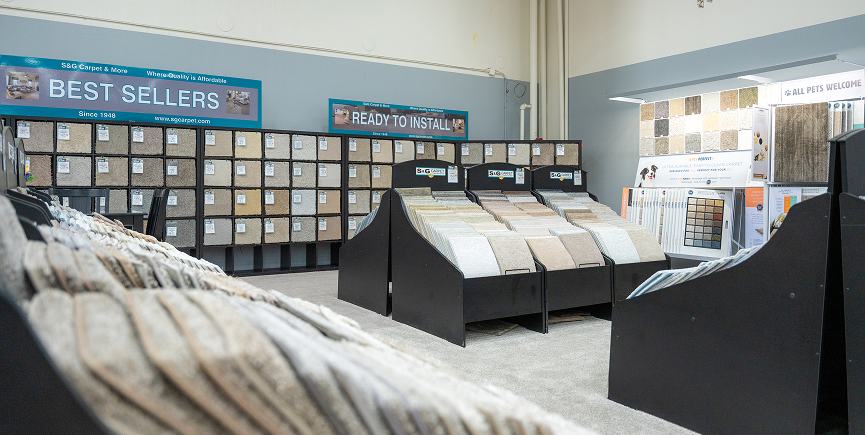 "Flooring sample boards on black display stands in an S&G Carpet showroom with Best Sellers and Ready to Install signs.