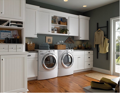 Medium brown wood flooring in a modern laundry room with white cabinets and appliances against a dark gray wall.