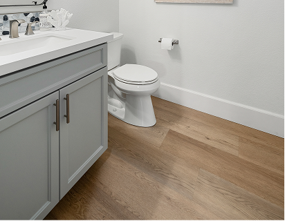 Light brown wood-look laminate flooring in a modern bathroom with a white vanity and toilet.
