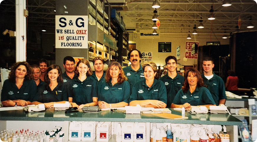 Vintage photo of the S&G Carpet team behind the store counter under a 'We Sell Only 1st Quality Flooring' sign
