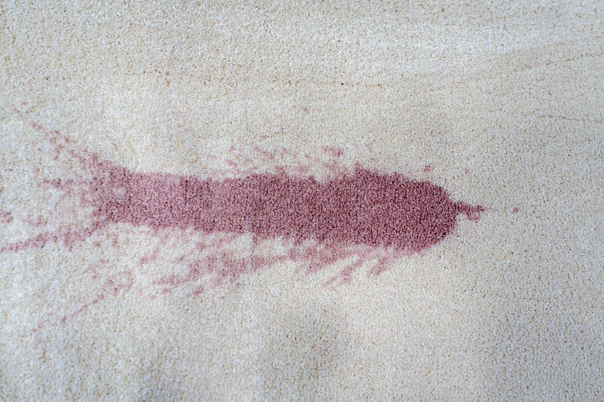 Close-up of a dark red spill stain soaked into beige textured carpet
