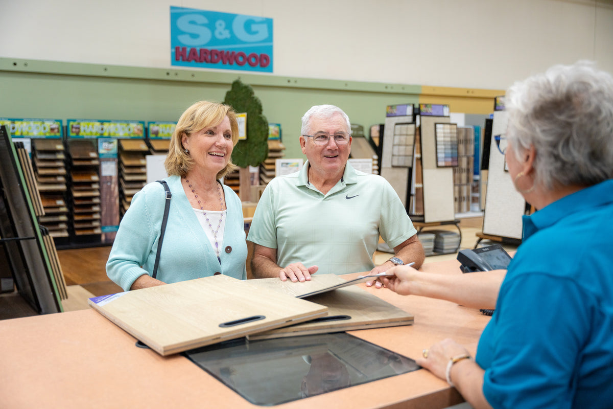 Couple at the counter with hardwood samples while an S&G associate helps them