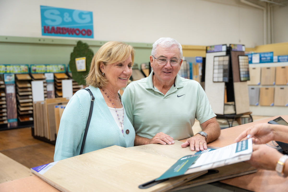 Couple reviewing hardwood flooring samples and a brochure with a sales associate at the S&G Carpet counter