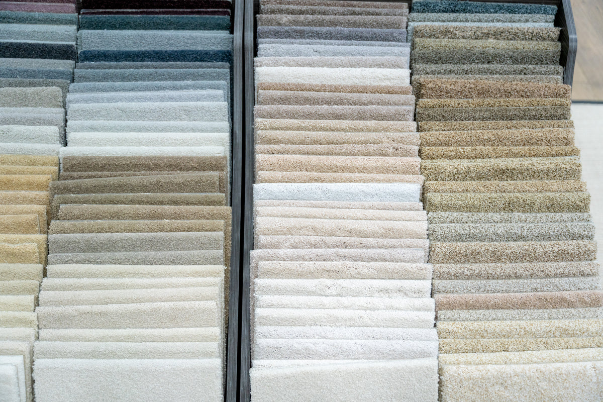 Three vertical columns of layered carpet samples in beige, gray, brown, and blue tones on a display rack.