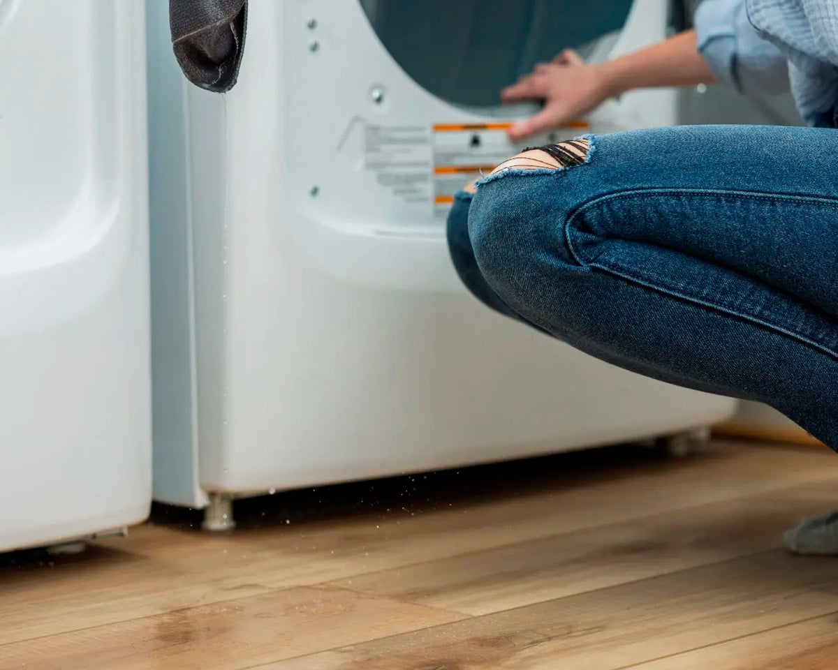 Person loading a washing machine on warm oak wood-look flooring in a laundry room