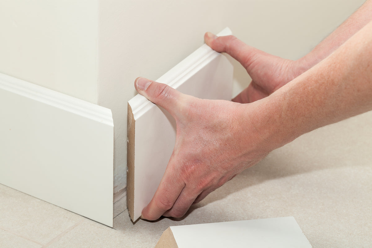 Installer fitting white baseboard trim against a wall above tile flooring