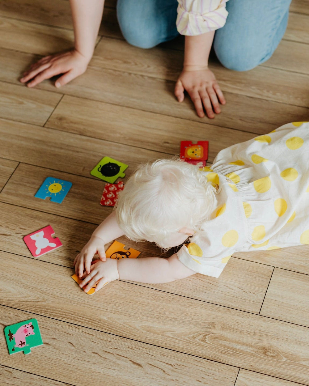 Toddler playing with colorful blocks on light wood-look laminate flooring next to an adult