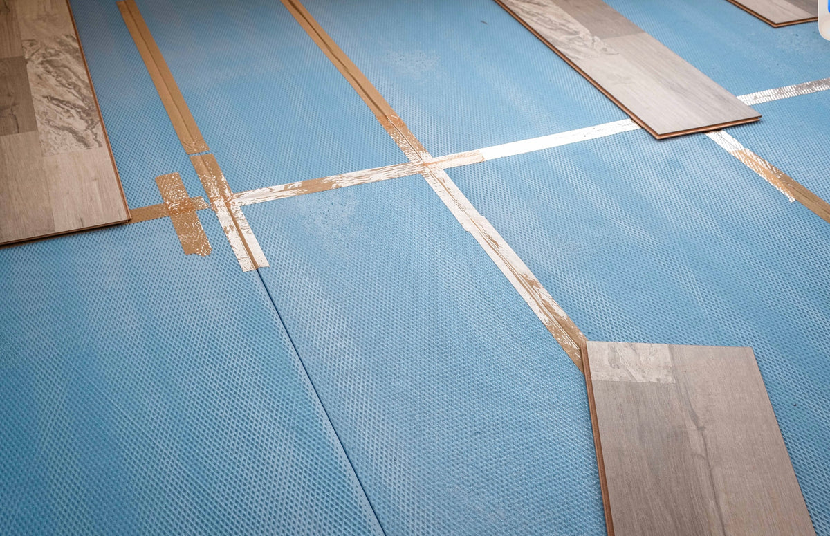 Wood-look laminate planks laid over blue foam underlayment during a flooring installation