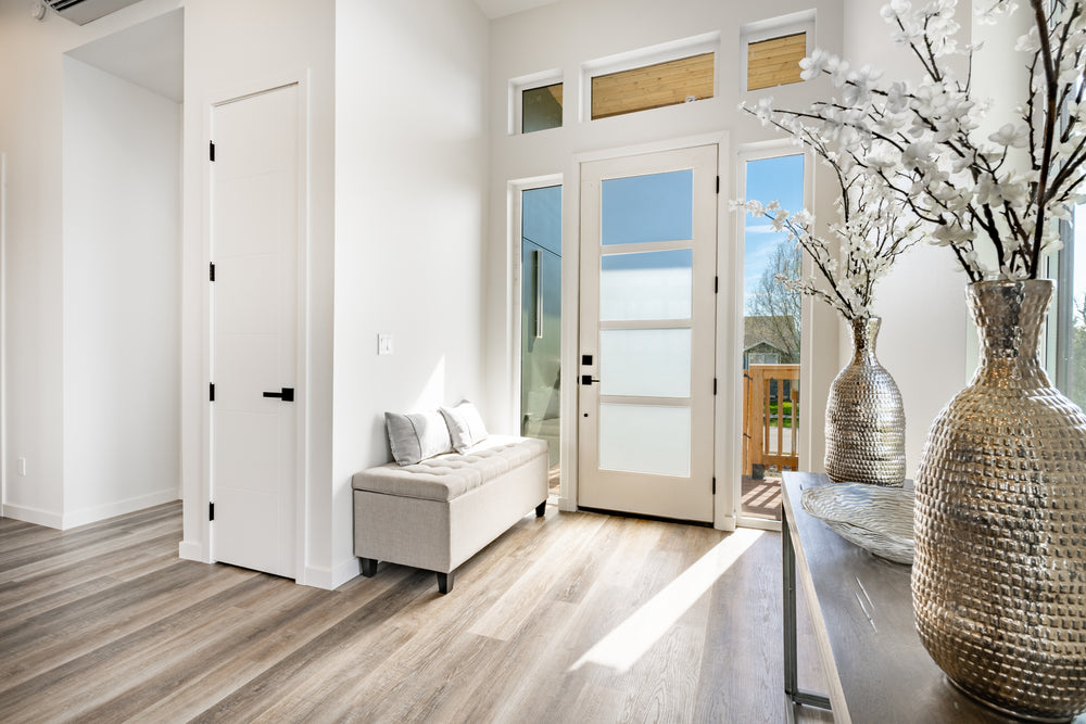 Gray-toned wood plank flooring in a bright entryway with a bench and frosted glass front door