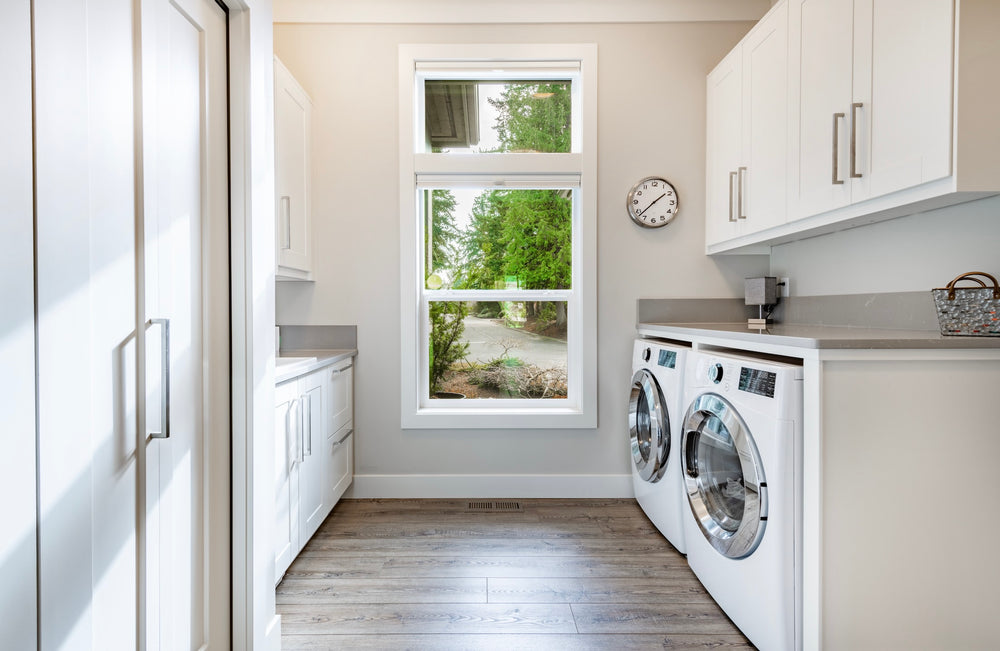 Wood plank flooring in a laundry room with white cabinets and a front-loading washer and dryer