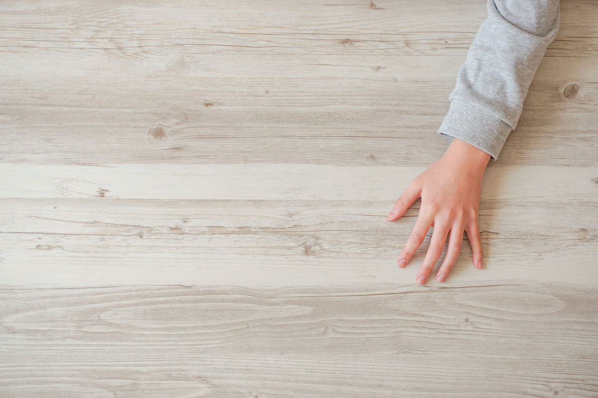 Hand resting on pale whitewashed wood plank flooring