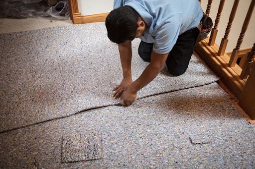 An installer seams wall-to-wall carpet near a wooden staircase during installation.