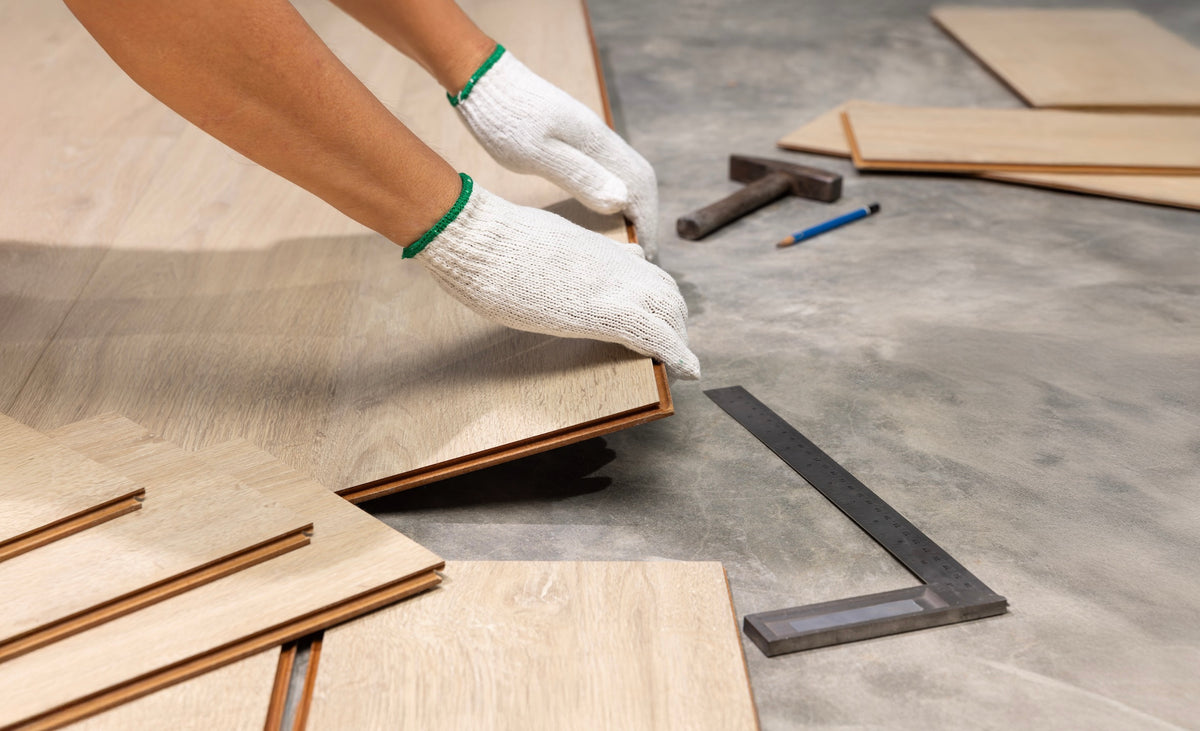 Gloved installer clicking a light oak laminate plank into place over a concrete subfloor