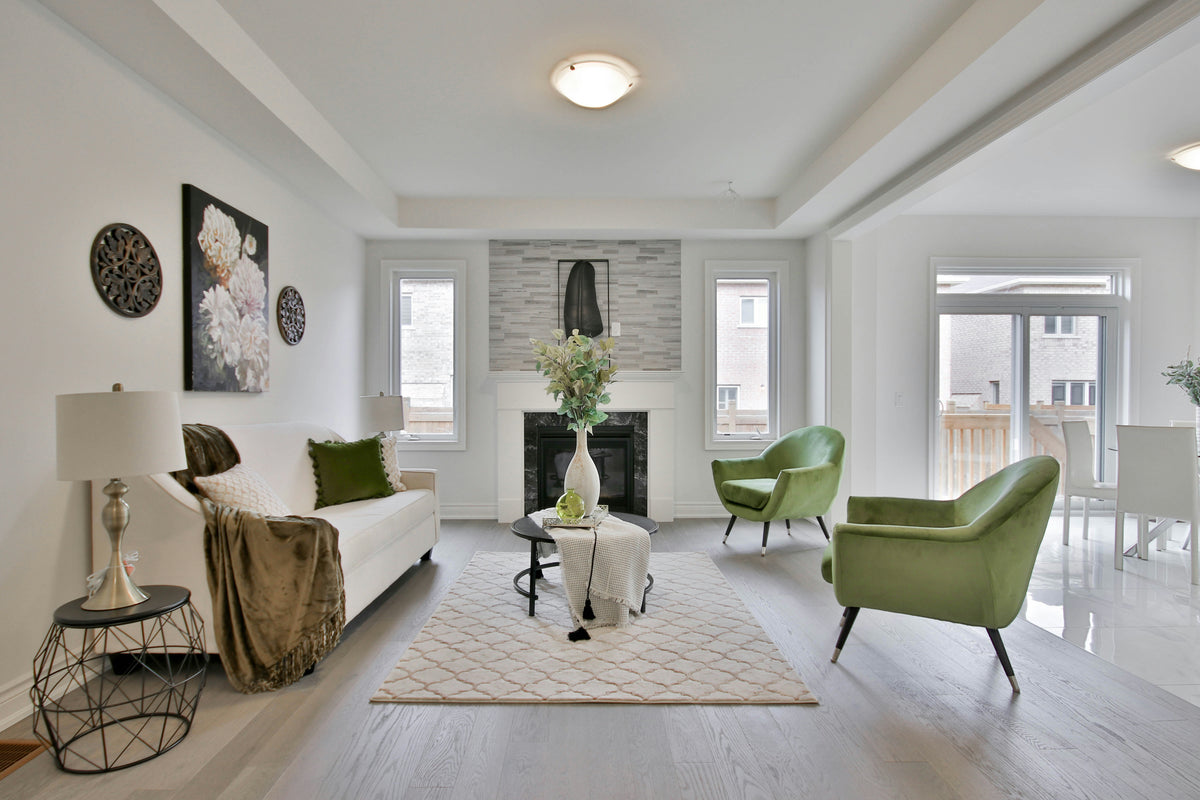 Pale gray wood plank flooring in a living room with green armchairs, a cream sofa, and area rug