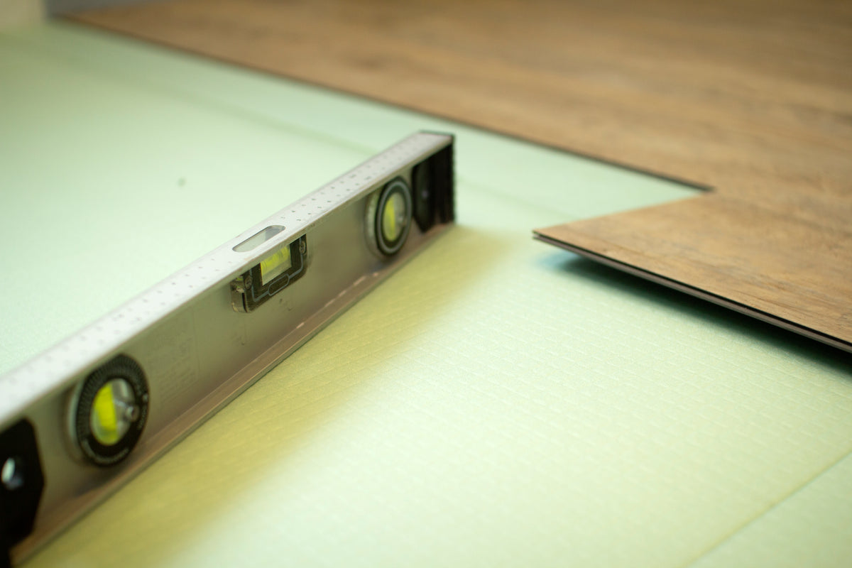 Spirit level and luxury vinyl plank on green underlayment during a flooring installation