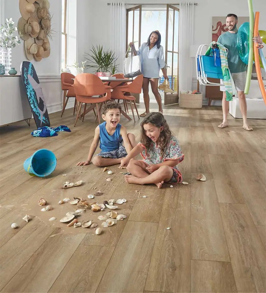 Children playing with shells on Mohawk light oak plank flooring as parents come in behind them