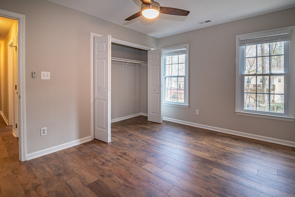 Dark brown hardwood plank flooring in an empty bedroom with beige walls, a closet, and a ceiling fan
