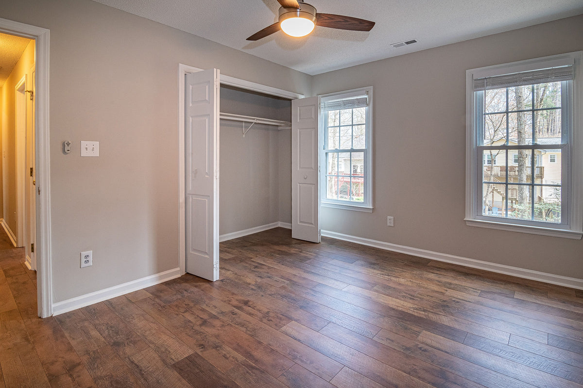 Dark brown hardwood plank flooring in an empty bedroom with beige walls, a closet, and a ceiling fan