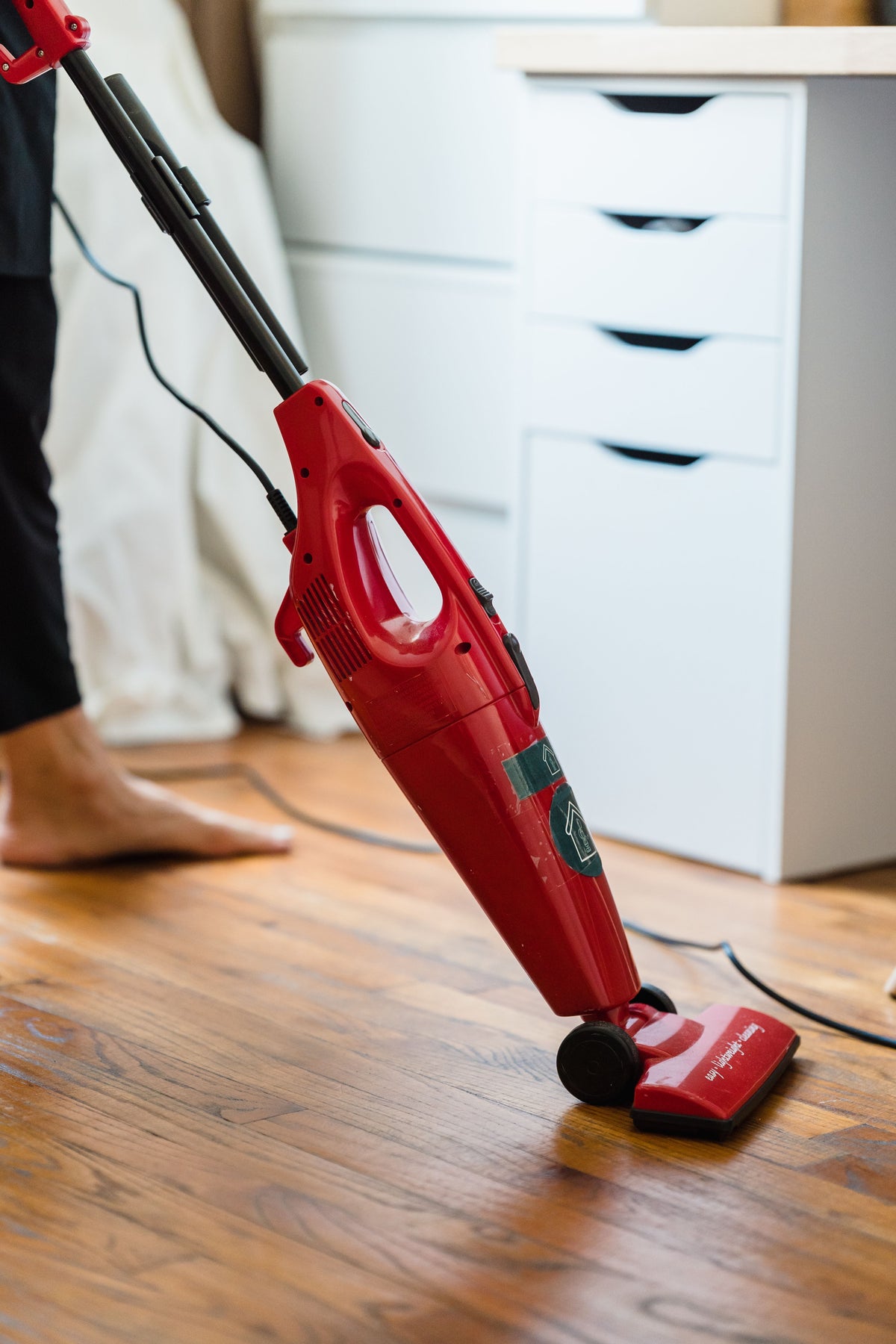 Red stick vacuum being used on medium brown hardwood plank flooring