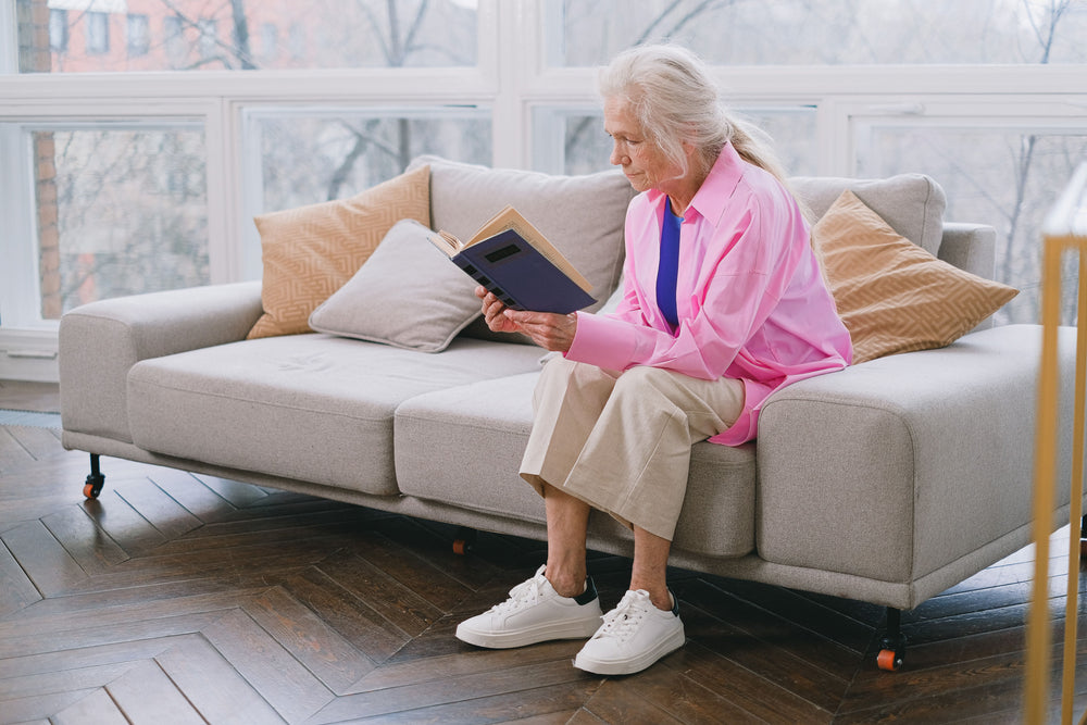 Dark chevron hardwood flooring in a bright living room where an older woman reads on a gray sofa
