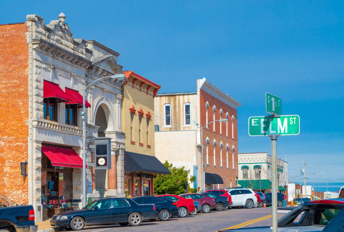 Historic brick storefronts on E Elm St in downtown Rogers, Arkansas, under a clear blue sky