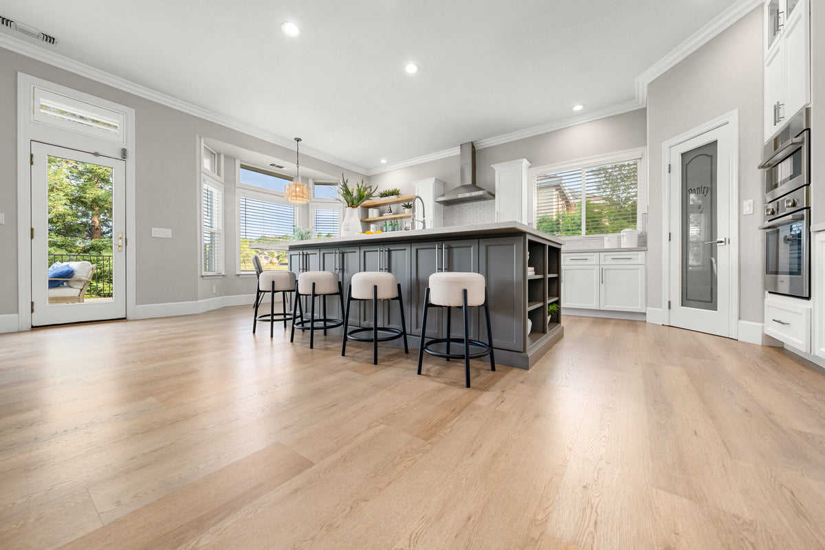 Wide-plank light oak flooring in an open kitchen with a gray island, bar stools, and white cabinets