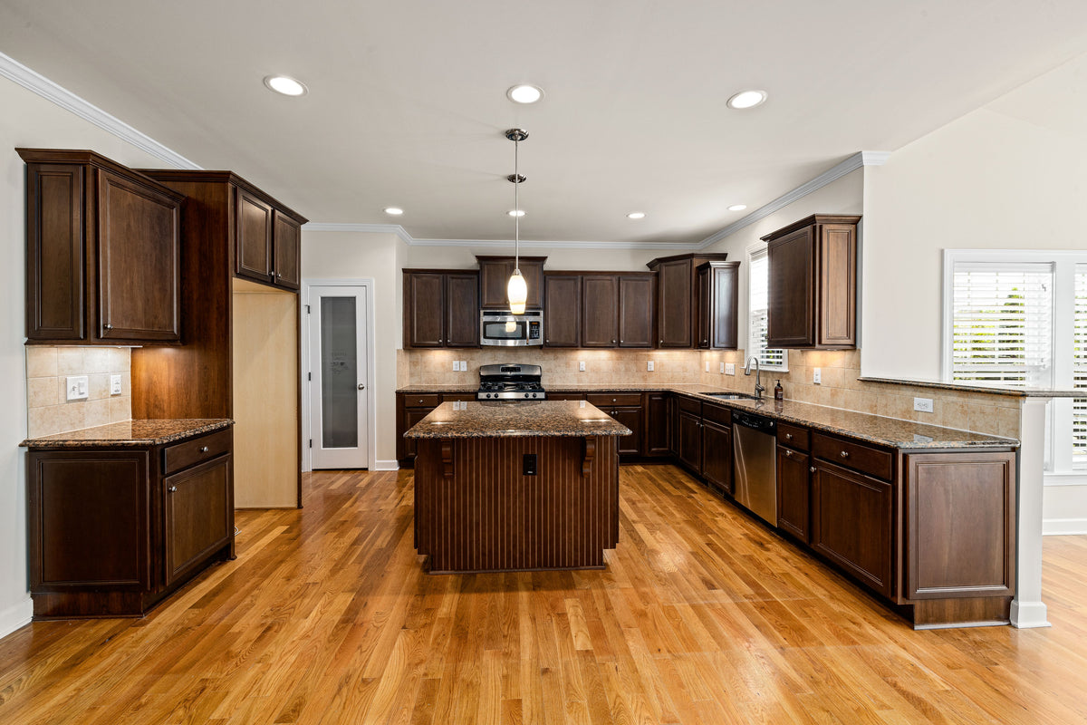 Golden oak wood-look flooring in a kitchen with dark cabinets, granite counters, and a center island
