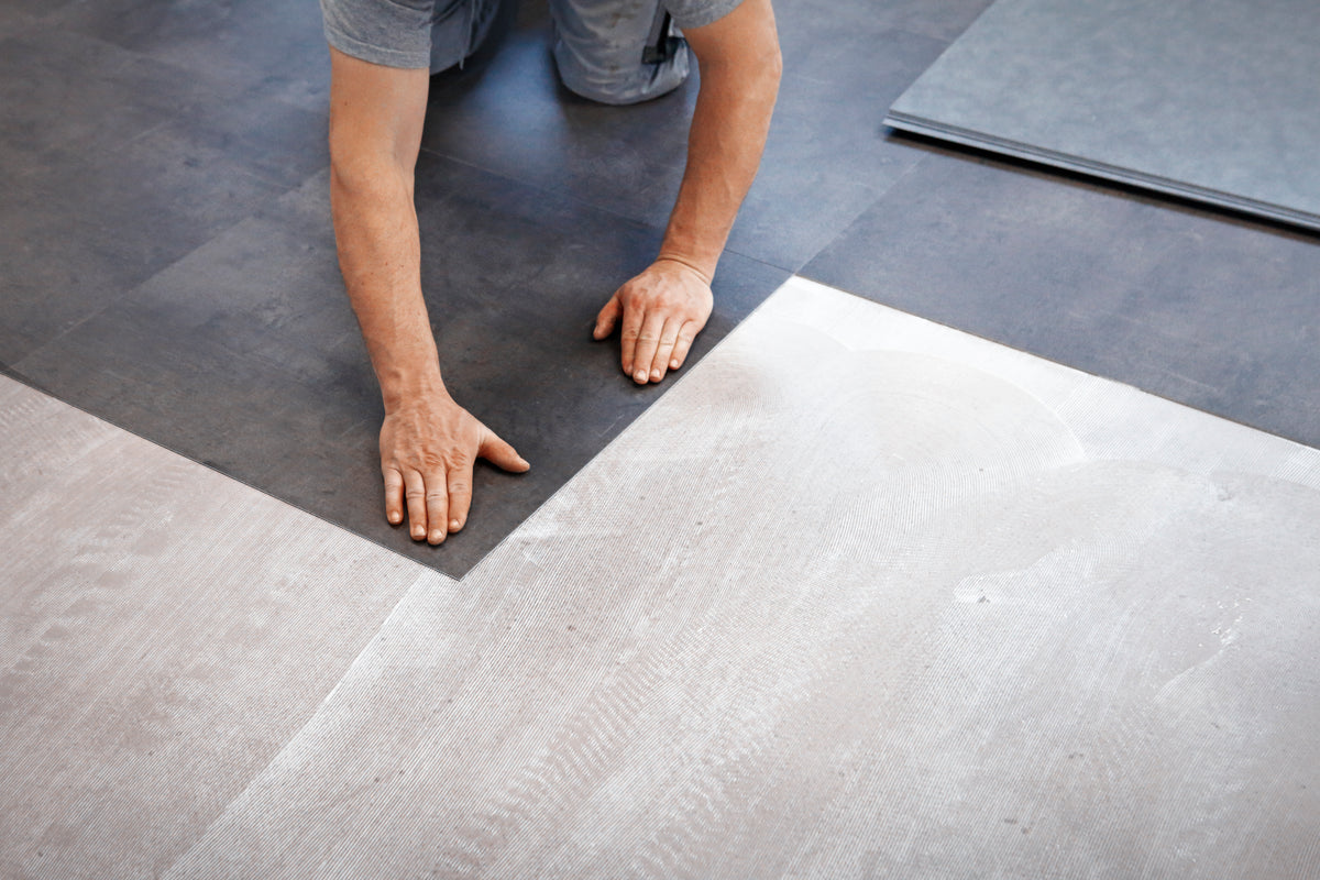 Installer smoothing a large gray vinyl floor tile into place over subfloor
