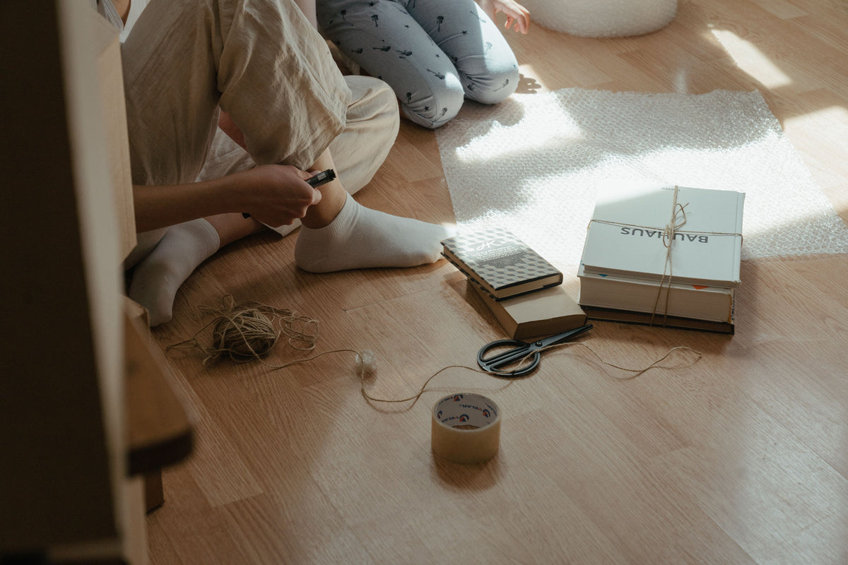 Light oak plank flooring in sunlight as two people sit wrapping packages with twine, scissors, and tape